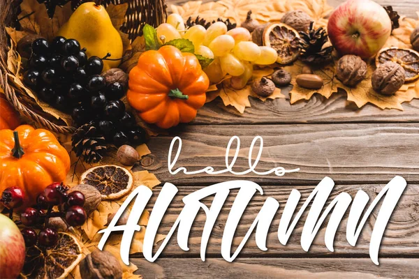 Autumnal harvest in basket on foliage near hello autumn lettering on wooden background — Stock Photo