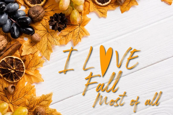 Top view of autumnal decoration and grapes near i love fall most of all lettering on white wooden background — Stock Photo