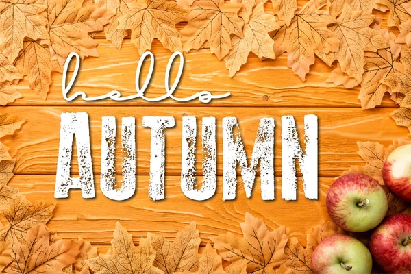 Top view of ripe apples and leaves near hello autumn lettering on wooden background — Stock Photo