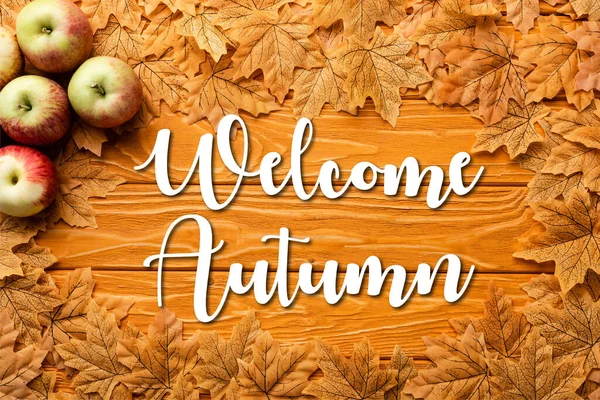 Vue de dessus des pommes mûres et feuillage de feuilles près de bienvenue lettrage d'automne sur fond en bois — Photo de stock