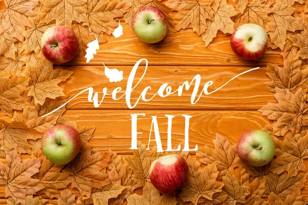 Vue de dessus des pommes mûres et des feuilles près du lettrage d'automne bienvenu sur fond en bois — Photo de stock