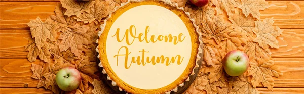 Vista superior del pastel de calabaza de acción de gracias con manzanas en hojas cerca de la bienvenida con letras de otoño sobre fondo de madera, cultivo panorámico - foto de stock