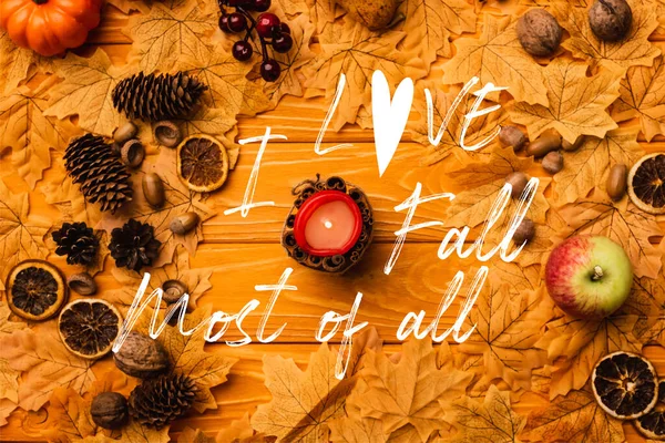 Draufsicht auf brennende Kerze mit herbstlicher Dekoration in der Nähe von I love fall am meisten Schriftzug auf Holzgrund — Stockfoto