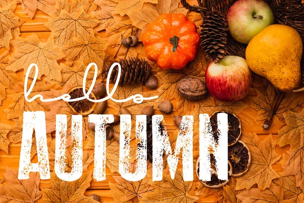 Top view of autumnal decoration and food scattered from wicker basket near hello autumn lettering on golden foliage — Stock Photo