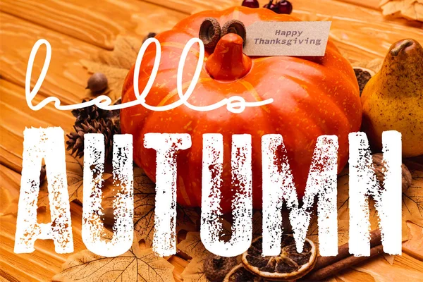 Calabaza con decoración otoñal y feliz tarjeta de acción de gracias cerca de hola letras de otoño sobre fondo de madera - foto de stock