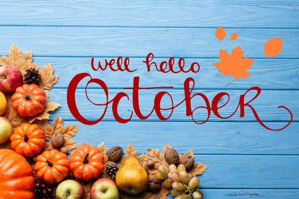 Top view of autumnal harvest and leaves near well hello october lettering on blue wooden background — Stock Photo