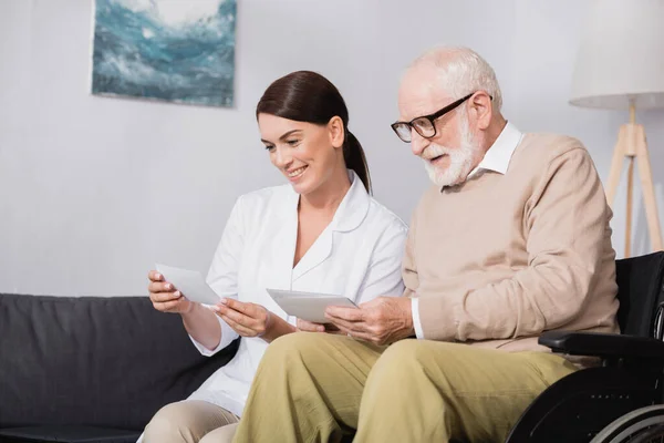 Cheerful elderly man and social worker looking at photos at home — Stock Photo