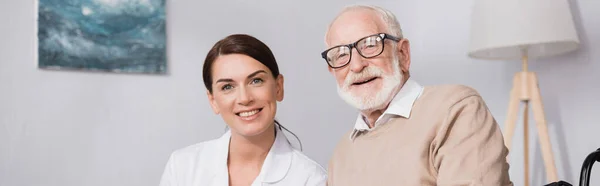 Smiling aged man near cheerful social worker looking at camera, banner — Stock Photo