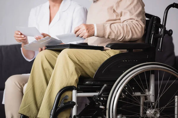 Cropped view of social worker showing family photos to handicapped man on blurred background — Stock Photo