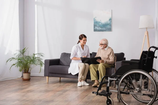 Geriatric nurse and elderly man browsing photo album on blurred foreground — Stock Photo