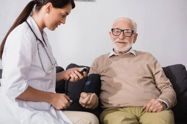 Collage d'infirmière gériatrique examinant homme âgé avec tonomètre à la maison — Photo de stock