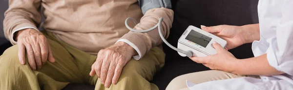 Infirmière gériatrique examen homme âgé avec tonomètre à la maison, bannière — Photo de stock