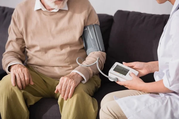 Cropped view of geriatric nurse examining aged man with tonometer at home — Stock Photo