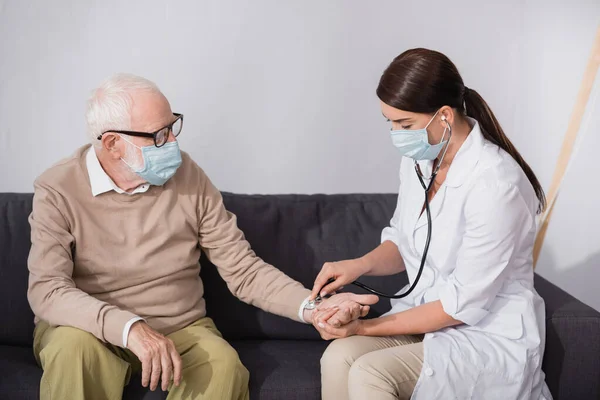 Brunette nurse checking pressure of aged man with stethoscope — Stock Photo