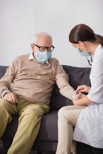 Collage einer Altenpflegerin, die einen älteren Mann zu Hause mit einem Stethoskop untersucht — Stockfoto
