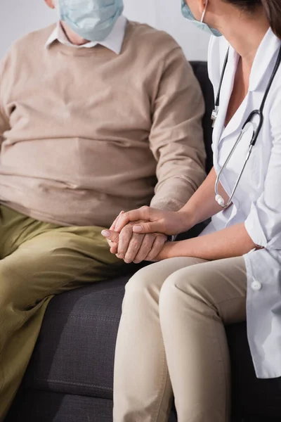 Vue recadrée de l'infirmière vérifiant la santé en se tenant la main avec un patient âgé — Photo de stock