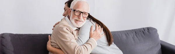 Elderly man smiling at camera while hugging adult daughter at home, banner — Stock Photo