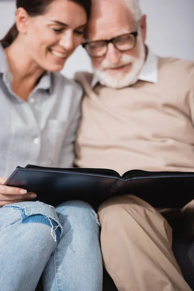 Adult woman with elderly father browsing photo album on blurred background — Stock Photo