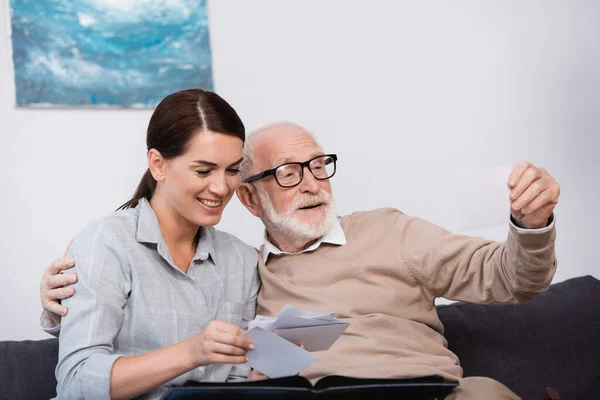 Donna sorridente con padre anziano guardando le foto di famiglia insieme a casa — Foto stock