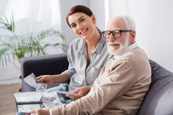 Smiling woman with elderly father looking at camera while looking at family photos together — Stock Photo