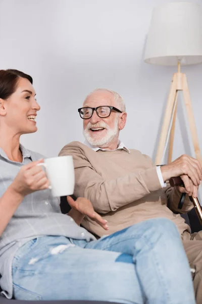 Donna sorridente che tiene il tè mentre parla con padre invecchiato in primo piano sfocato — Foto stock
