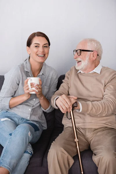 Mulher animada segurando xícara de chá enquanto conversa com pai sorridente envelhecido — Fotografia de Stock