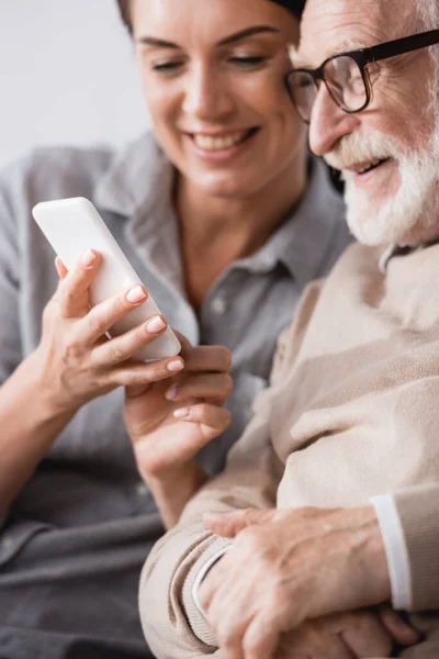 Fröhliche Frau plaudert auf Smartphone neben glücklichem Papa auf verschwommenem Hintergrund — Stockfoto