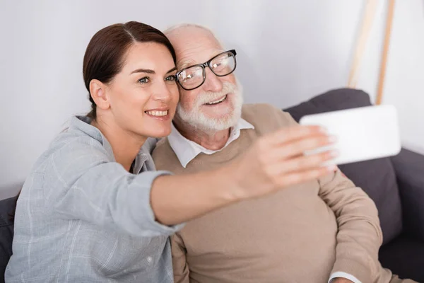 Glückliche Frau und älterer Mann machen Selfie mit Handy im verschwommenen Vordergrund — Stockfoto