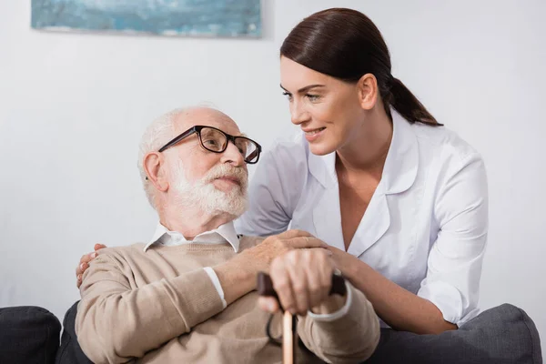 Enfermera geriátrica y hombre anciano mirándose en casa - foto de stock