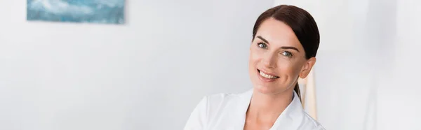 Infirmière brune joyeuse en manteau blanc souriant à la caméra, bannière — Photo de stock