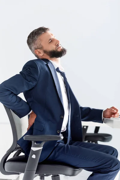 Businessman in formal wear suffering from back pain near table in office — Stock Photo