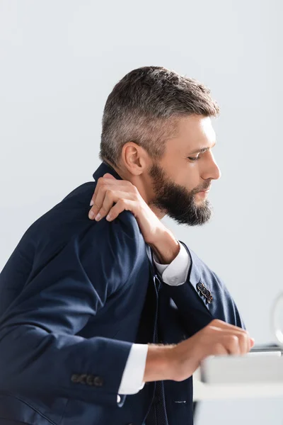 Vista lateral del hombre de negocios en traje sintiendo dolor de hombro cerca del primer plano borroso en la oficina - foto de stock