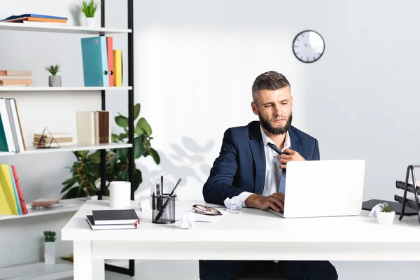 Businessman feeling hot while working on laptop near stationery in office — Stock Photo