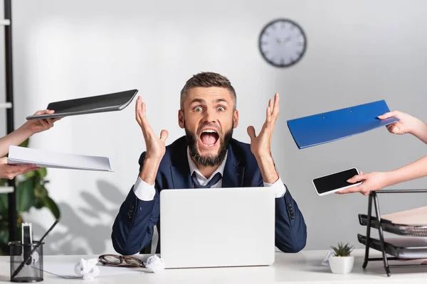 Stressed businessman screaming near colleagues with paper folders and gadgets in office — Stock Photo