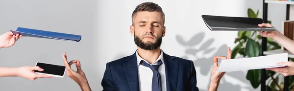 Businessman meditating near colleagues with smartphone and paper folders in office, banner — Stock Photo