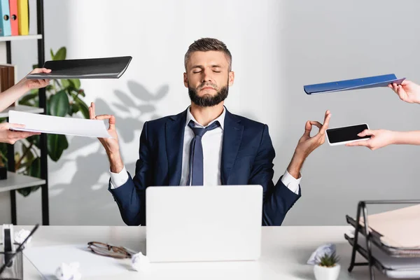 Empresário meditando perto de colegas com documentos e gadgets em primeiro plano desfocado no escritório — Fotografia de Stock