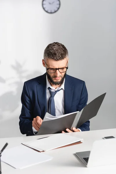 Homme d'affaires tenant dossier papier près de gadgets sur le premier plan flou dans le bureau — Photo de stock