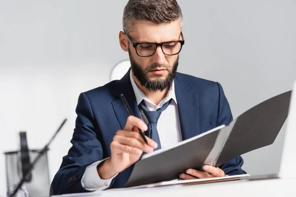 Uomo d'affari in occhiali che tiene cartellina di carta e penna in primo piano sfocato in ufficio — Foto stock