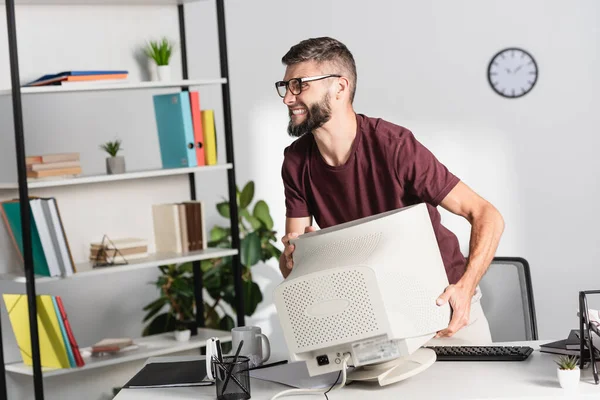 Разгневанный бизнесмен держит монитор компьютера во время нервного срыва в офисе — стоковое фото