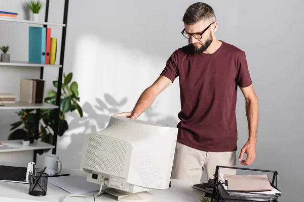 Geschäftsmann in Freizeitkleidung berührt Computermonitor neben Schreibwaren auf Tisch — Stockfoto