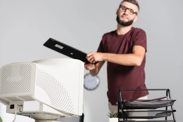 Computermonitor und Papiere auf dem Tisch mit gestresstem Geschäftsmann mit Tastatur auf verschwommenem Hintergrund — Stockfoto