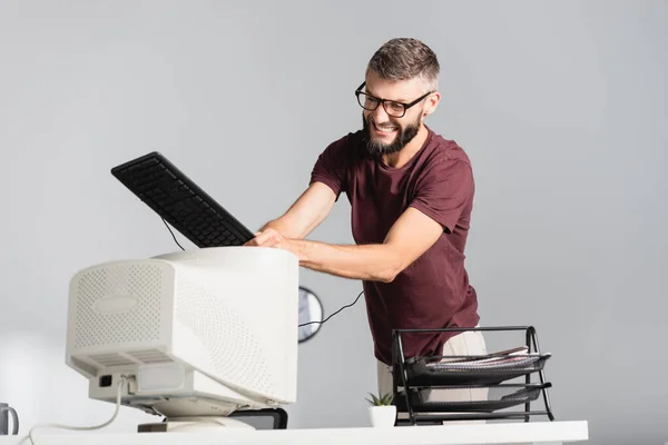Loco hombre de negocios con teclado golpeando monitor de computadora en primer plano borroso en la oficina - foto de stock