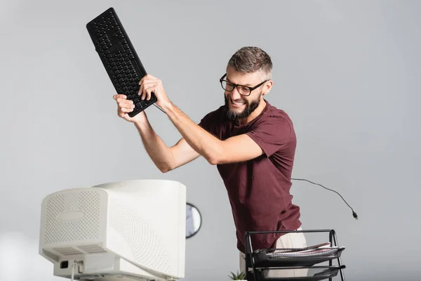 Nervous businessman holding computer keyboard near monitor on blurred foreground in office — Stock Photo