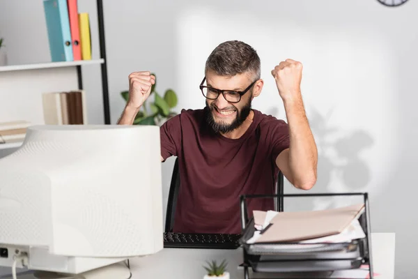 Enojado hombre de negocios con las manos en los puños mirando la computadora cerca de papeles en primer plano borrosa - foto de stock