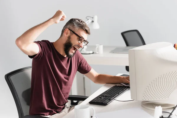 Hombre de negocios gritando sentado cerca de la computadora en primer plano borroso durante la crisis nerviosa en la oficina - foto de stock