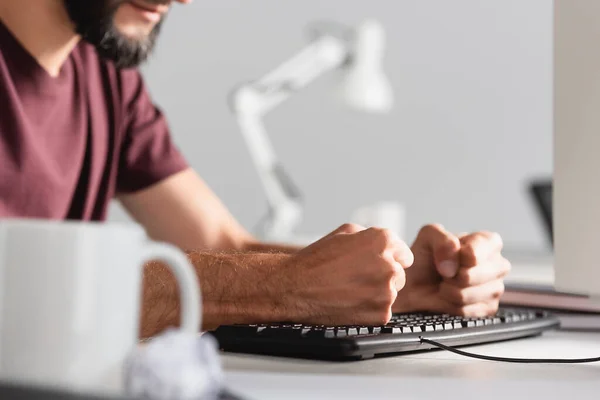 Cropped view of stressed businessman beating computer keyboard with cup and clumped paper on blurred foreground — Stock Photo