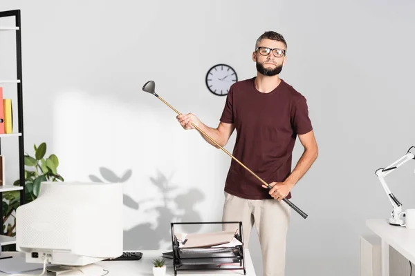 Empresario sosteniendo club de golf cerca de la computadora en primer plano borroso en la oficina - foto de stock