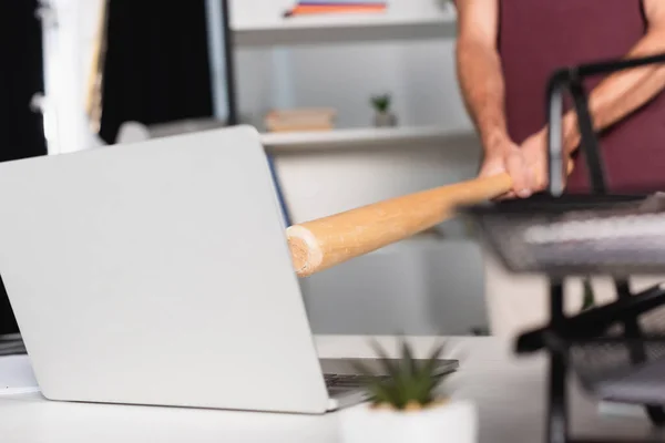 Vista cortada do homem de negócios segurando bastão de beisebol perto do laptop com primeiro plano borrado na mesa do escritório — Fotografia de Stock