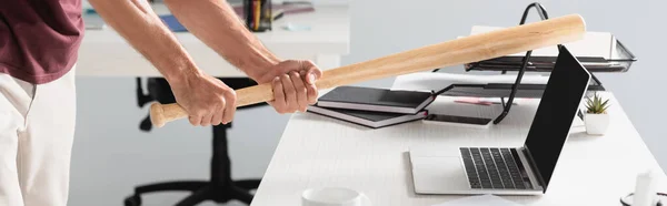 Cropped view of businessman beating laptop with baseball bat with blurred background in office, banner — Stock Photo