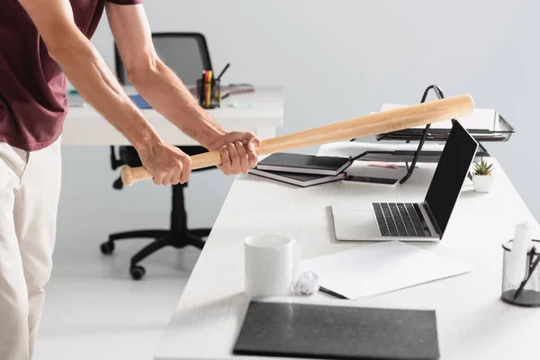 Vista cortada do empresário batendo laptop com bastão de beisebol perto da pasta de papel em primeiro plano desfocado — Fotografia de Stock